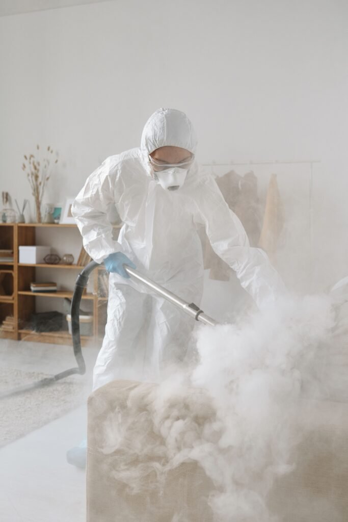 Person in a hazmat suit using equipment to disinfect a room, indoors.