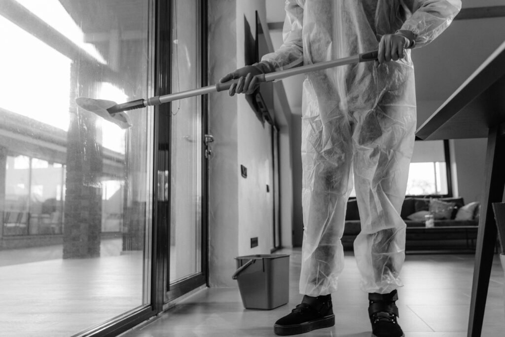 A person in a protective suit cleans glass doors indoors, emphasizing hygiene.